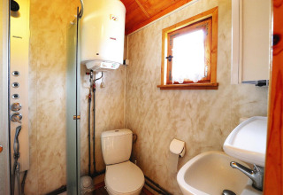 Baño de cabaña pequeño con inodoro, lavabo, calentador de agua, ducha y una ventana con cortina.