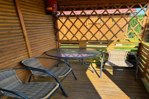 Wooden porch with glass table and three chairs at Single-storey cottages Jarosławiec, sunny day in Denmark.