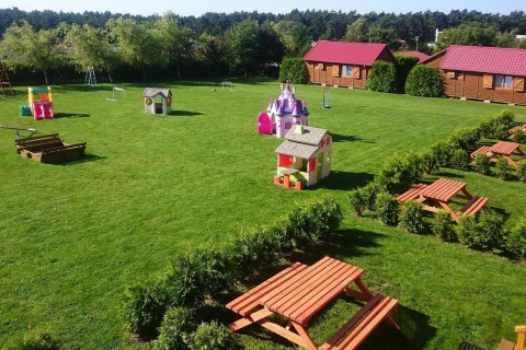 Speelplaats en picknicktafels voor gelijkvloerse huisjes met rode daken in Jarosławiec, omgeven door groen.