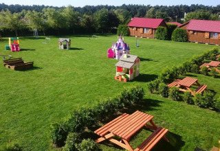 Speelplaats en picknicktafels voor gelijkvloerse huisjes met rode daken in Jarosławiec, omgeven door groen.