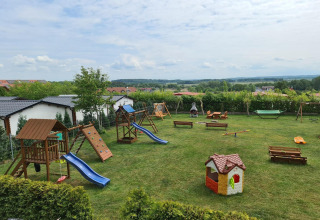 Playground at single-storey cottages Jarosławiec featuring slides, swings, benches, and scenic grassy area.