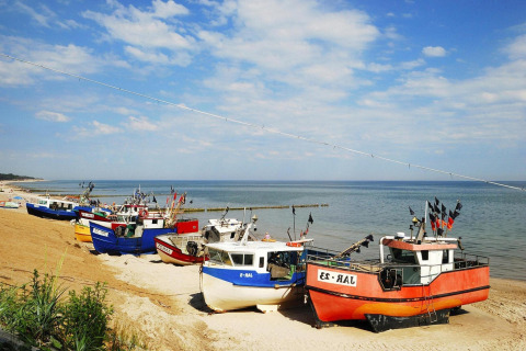 Colorful fishing boats lined up on the sandy beach under a blue sky in Jarosławiec, Denmark.