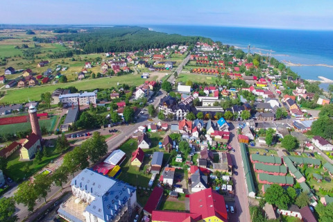 Luchtfoto van Jarosławiec met gelijkvloerse huisjes, groene zones en de Baltische kust op de achtergrond.
