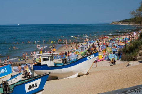 Crowded beach in Jarosławiec with fishing boats, umbrellas, and sunbathers near the Baltic Sea.