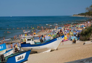 Crowded beach in Jarosławiec with fishing boats, umbrellas, and sunbathers near the Baltic Sea.