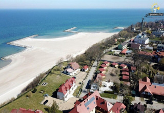Aerial view of beach, sea, and cottages in Jarosławiec, not Denmark, with a sandy shoreline and homes nearby.