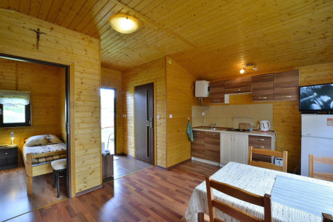 Interior of Holiday cottage Rusinowo featuring wood paneling, a bedroom, kitchen area, and dining table.