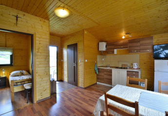 Interior de la cabaña Holiday cottage Rusinowo con paredes de madera, dormitorio, cocina y mesa comedor.