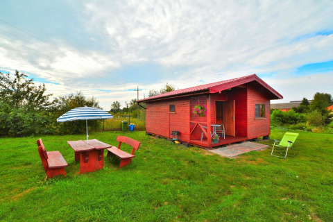 Vakantiehuis Rusinowo: houten chalet met tuinmeubilair, parasol en ligstoel op een groen grasveld.
