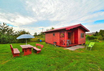 Cabaña de madera Holiday cottage Rusinowo con muebles de jardín y sombrilla sobre césped verde.