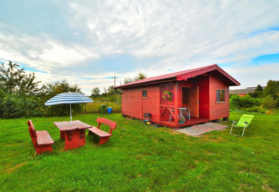 Casa vacanze Rusinowo: casetta di legno rossa, arredo da giardino e ombrellone su prato verde.