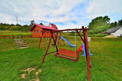 Playground with swing, slide, and wooden cottage on grass near Holiday cottage Rusinowo in Denmark.