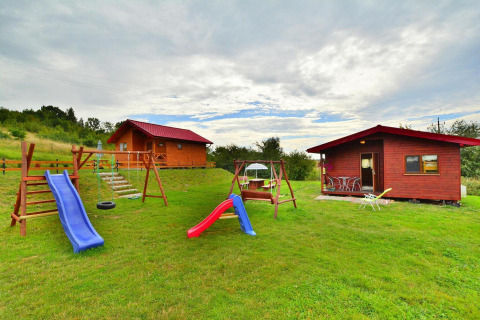 Udendørs foto af Holiday cottage Rusinowo, med to hytter, legeplads og grønt græs under en overskyet himmel.