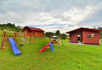 Vista exterior de Holiday cottage Rusinowo con dos cabañas de madera, parque infantil y césped bajo cielo nublado.