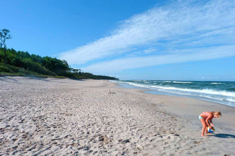 Bambina che gioca con una palla sulla spiaggia di sabbia vicino al cottage Rusinowo, mare e foresta sullo sfondo.