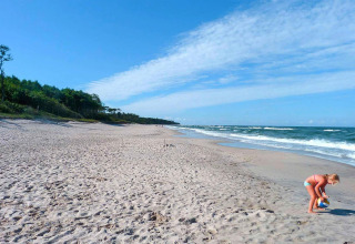 Child playing with a ball on a quiet sandy beach near Holiday cottage Rusinowo, with sea and forest in the background.