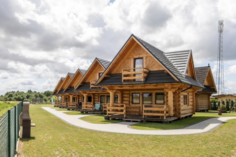 Rij houten huisjes bij Highlander cottages ZUMAR Wicie, Denemarken, met grasvelden en bewolkte hemel.
