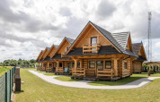 Rij houten huisjes bij Highlander cottages ZUMAR Wicie, Denemarken, met grasvelden en bewolkte hemel.