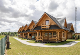 Row of wooden lodges at Highlander cottages ZUMAR Wicie, Denmark, with green lawns and a partly cloudy sky.