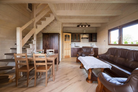 Sfeervol lodge-interieur met houten meubelen, lederen zithoek, open keuken en trap op de achtergrond.