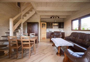 Gezellige lodge met houten eettafel, leren bankstel, keuken en trap in een licht houten interieur.
