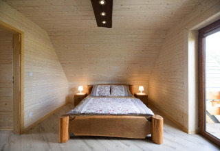 Slaapkamer met houten wanden in Highlander cottages ZUMAR Wicie in Denemarken, tweepersoonsbed en lampen.