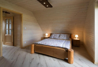 Slaapkamer met houten bekleding, tweepersoonsbed en twee nachtkastjes in Highlander cottages ZUMAR Wicie, Denemarken.