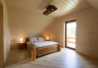 Dormitorio en Highlander cottages ZUMAR Wicie, Dinamarca, con paredes de madera, cama doble y acceso al balcón.
