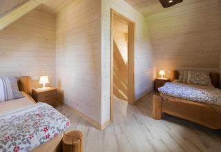 Two cozy bedrooms with wooden walls and single beds at Highlander cottages ZUMAR Wicie, Denmark.