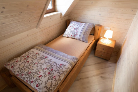 Gezellige houten slaapkamer met eenpersoonsbed, nachtkastje en lamp in Highlander cottages ZUMAR Wicie.