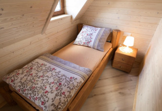Gezellige houten slaapkamer met eenpersoonsbed, nachtkastje en lamp in Highlander cottages ZUMAR Wicie.