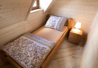 Gezellige houten slaapkamer met eenpersoonsbed, nachtkastje en lamp in Highlander cottages ZUMAR Wicie.