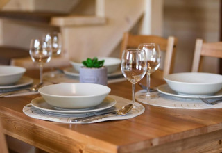 Set dining table for four at Highlander cottages ZUMAR Wicie, Denmark, with plates, wine glasses and cutlery.