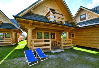 Log cabin at Highlander cottages ZUMAR Wicie in Denmark, featuring a porch and two blue deck chairs outside.