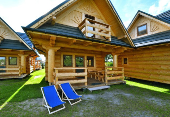 Log cabin at Highlander cottages ZUMAR Wicie in Denmark, featuring a porch and two blue deck chairs outside.