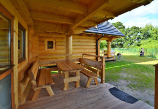 Wooden porch with benches and table at Highlander cottages ZUMAR Wicie in Denmark on a sunny day.