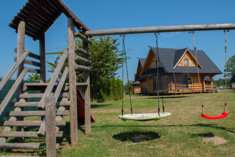 Playground with swings and a wooden lodge house on a grassy field at Highlander cottages ZUMAR Wicie in Denmark.