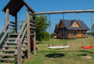 Playground with swings and a wooden lodge house on a grassy field at Highlander cottages ZUMAR Wicie in Denmark.