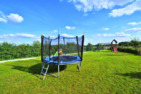 Outdoor playground with trampoline and slide at Highlander cottages ZUMAR Wicie, sunny day in Denmark.