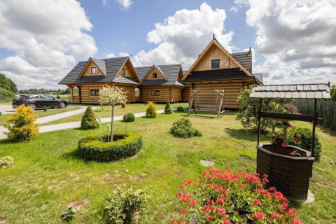 Afbeelding van Highlander cottages ZUMAR Wicie in Denemarken met blokhutten, tuin, bloemen en een waterput.