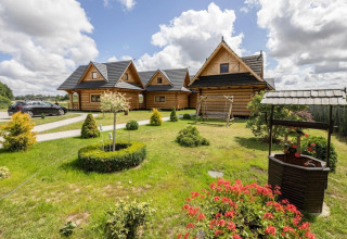 Photo of Highlander cottages ZUMAR Wicie in Denmark featuring log cabins, green lawn, well, and garden flowers.