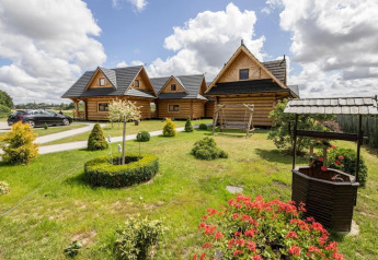Foto van Highlander cottages ZUMAR Wicie in Denemarken met houten huisjes, tuin, waterput en bloemen.