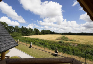 Zicht vanaf Highlander cottages ZUMAR Wicie in Denemarken, met velden, bomen en blauwe lucht met wolken.