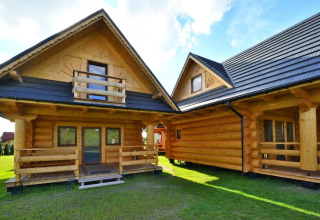 Two rustic log cabins with wooden balconies and a grassy yard at Highlander cottages ZUMAR Wicie, Denmark.