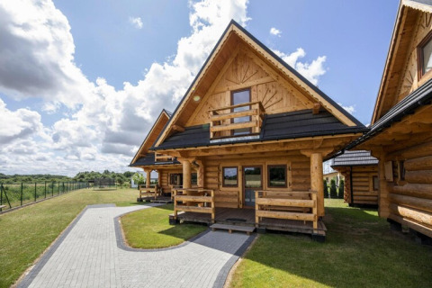 Log cabins at Highlander cottages ZUMAR Wicie in Denmark, featuring clear skies and grassy areas.
