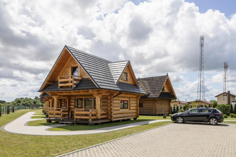 Blokhutten en zwarte auto bij Highlander cottages ZUMAR Wicie, met bewolkte hemel erboven.