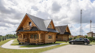 Cabañas de madera y coche negro en Highlander cottages ZUMAR Wicie, bajo un cielo nublado.