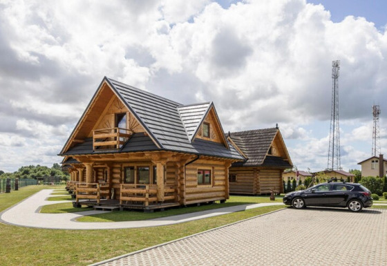 Blokhutten en zwarte auto bij Highlander cottages ZUMAR Wicie, met bewolkte hemel erboven.