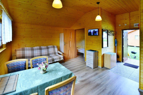 Vista interior de una acogedora cabaña de madera con mesa de comedor, sofá y dormitorio abierto.