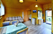 Vista interior de una acogedora cabaña de madera con mesa de comedor, sofá y dormitorio abierto.